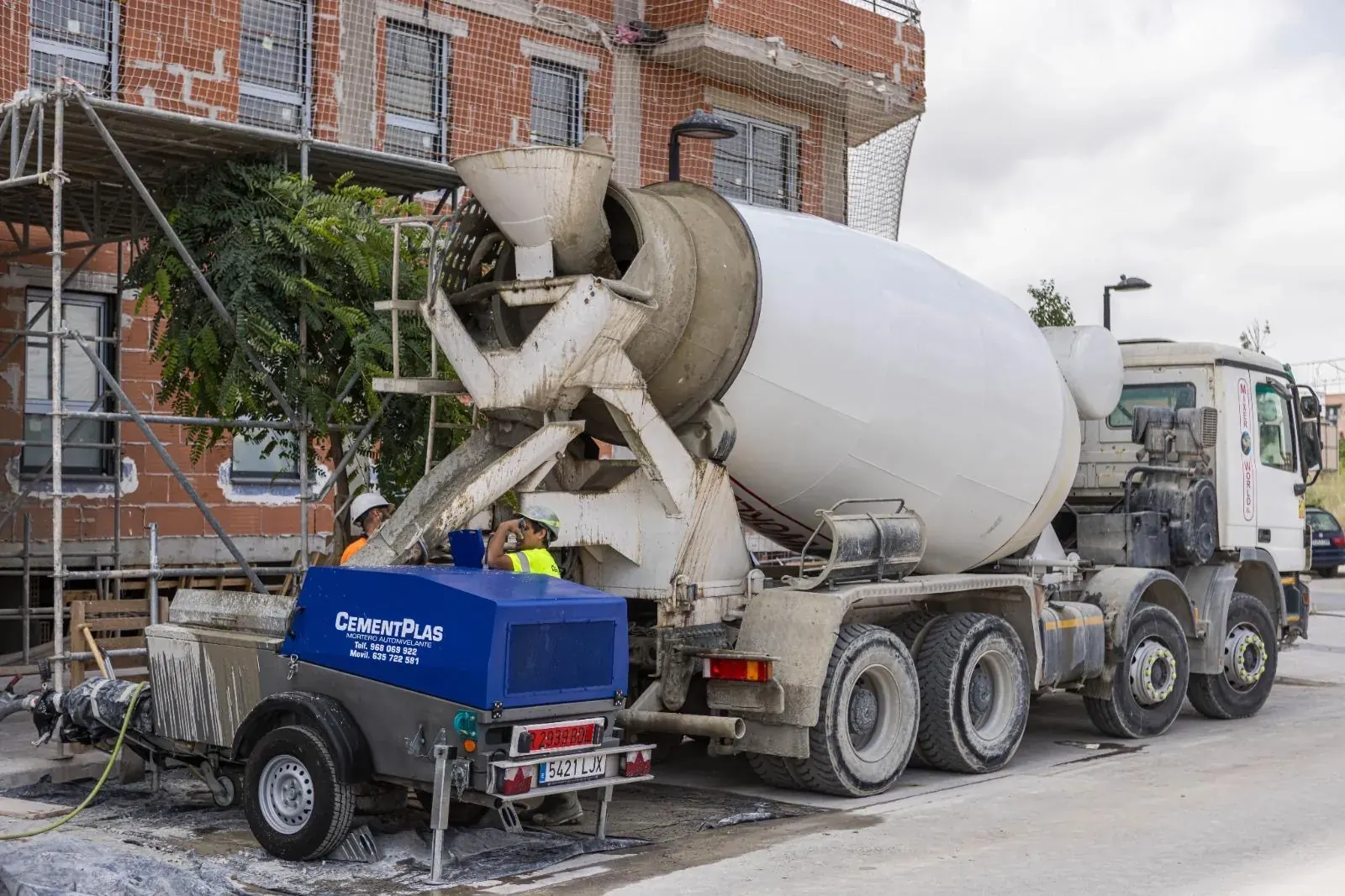 Camión hormigonera y bomba de hormigón junto a una obra de edificación